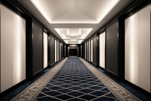 A sleek, symmetrical hotel hallway with black doors, glowing wall panels, recessed ceiling lights, and a blue diamond-patterned carpet.