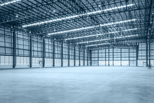 Spacious empty warehouse with steel beams, bright overhead lights, tall windows, and polished concrete floors in a cool blue, calm industrial setting.