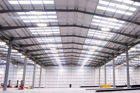 Spacious, empty industrial warehouse with steel beams, skylights, white walls, and loading equipment, conveying a clean, bright atmosphere.