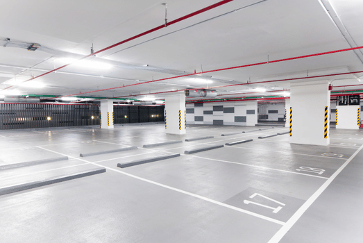 Bright, spacious underground parking garage with empty marked spaces, white columns, red ceiling pipes, and a clean, modern atmosphere.