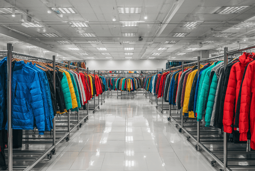 Bright clothing warehouse aisle lined with colorful puffer jackets—blue, red, teal, and yellow—arranged in neat, orderly rows.